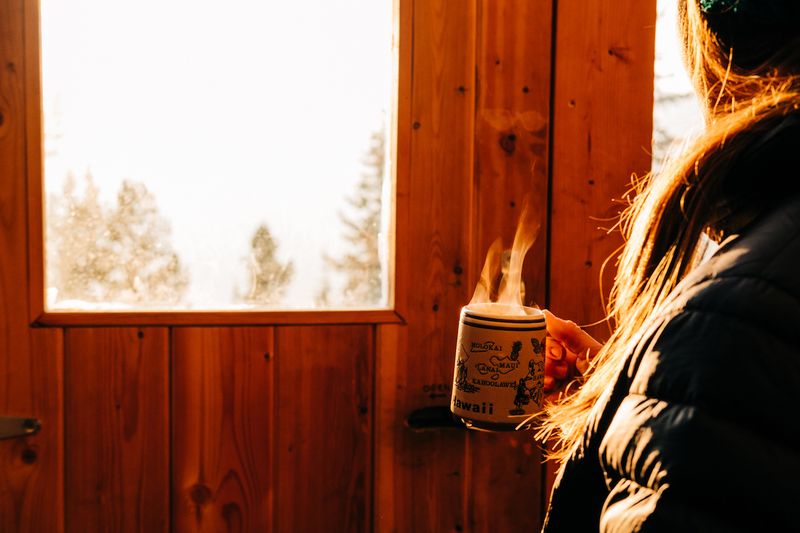 A woman stands in the Big Belt Hut doorway with coffee.