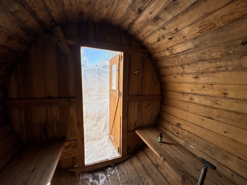 Wood-lined interior of the Big Belt Hut sauna with its door open to deep snow