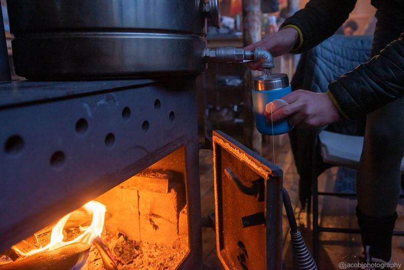 Person filling a cup with water from a snow melt pot on top of the woodstove.