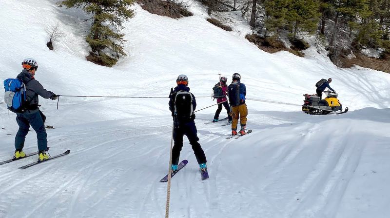 Skiers hold onto a rope behind a snowmobile on their way into YurtSki